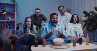 在电视上看<strong>体育比赛</strong>的时候，一个快乐的美国男人在旁边庆祝朋友的难过。 一群坐在沙发上的朋友